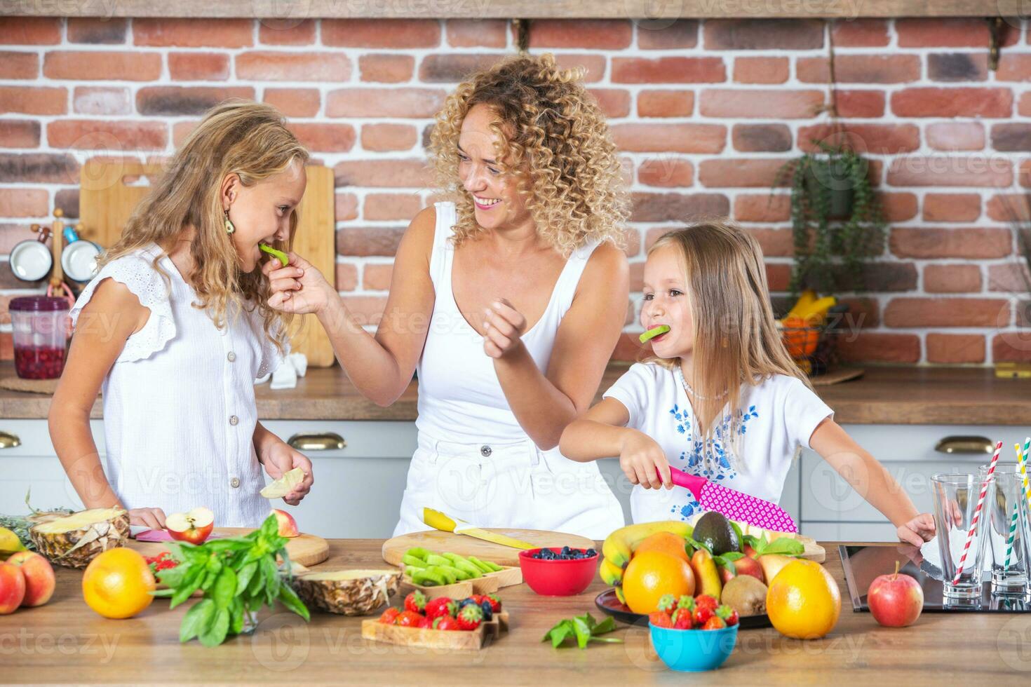 Mother and daughters cooking together in the kitchen. Healthy food concept. Portrait of happy family with fresh smoothies. Happy sisters. photo