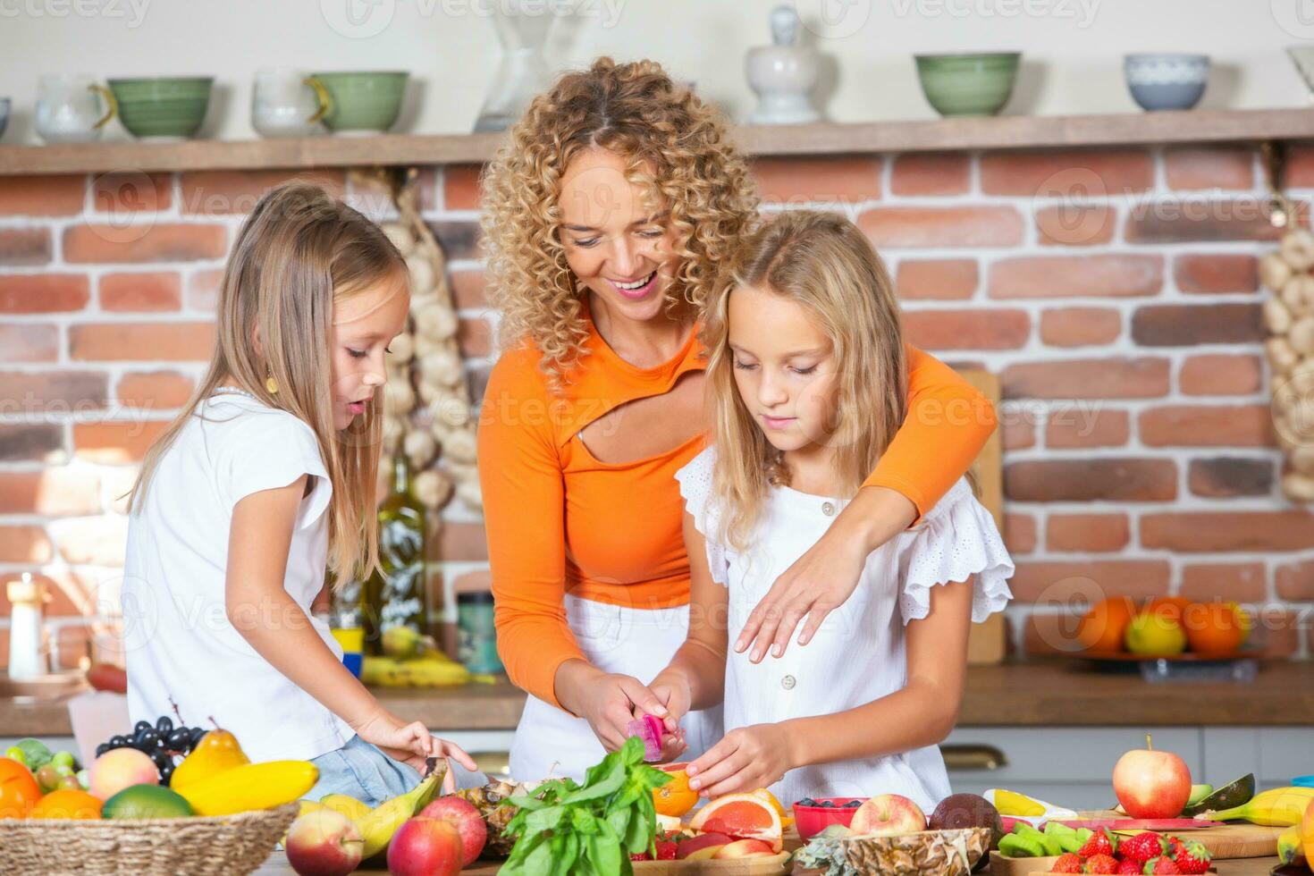 Mother and daughters cooking together in the kitchen. Healthy food concept. Portrait of happy family with fresh smoothies. Happy sisters. photo