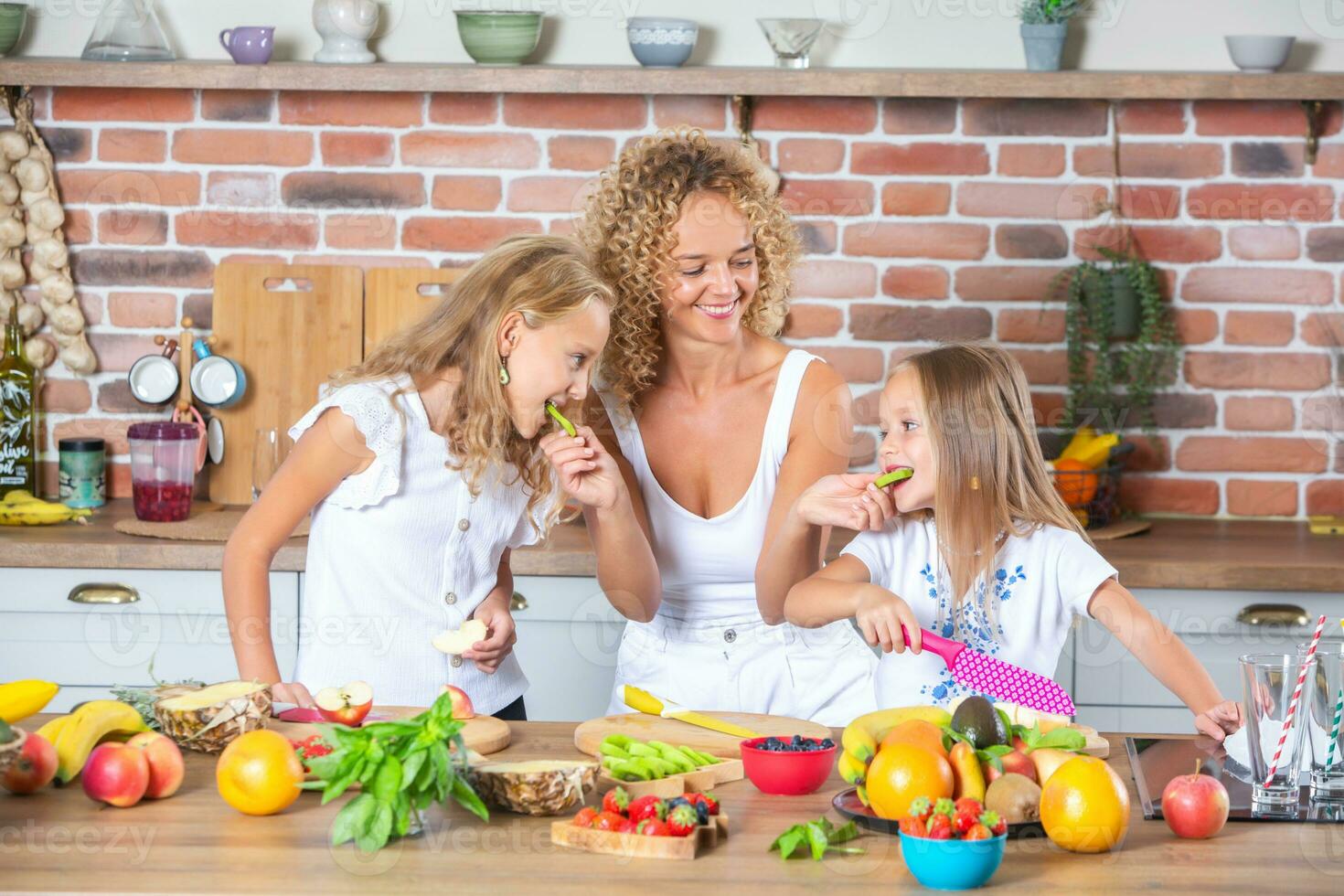 Mother and daughters cooking together in the kitchen. Healthy food concept. Portrait of happy family with fresh smoothies. Happy sisters. photo