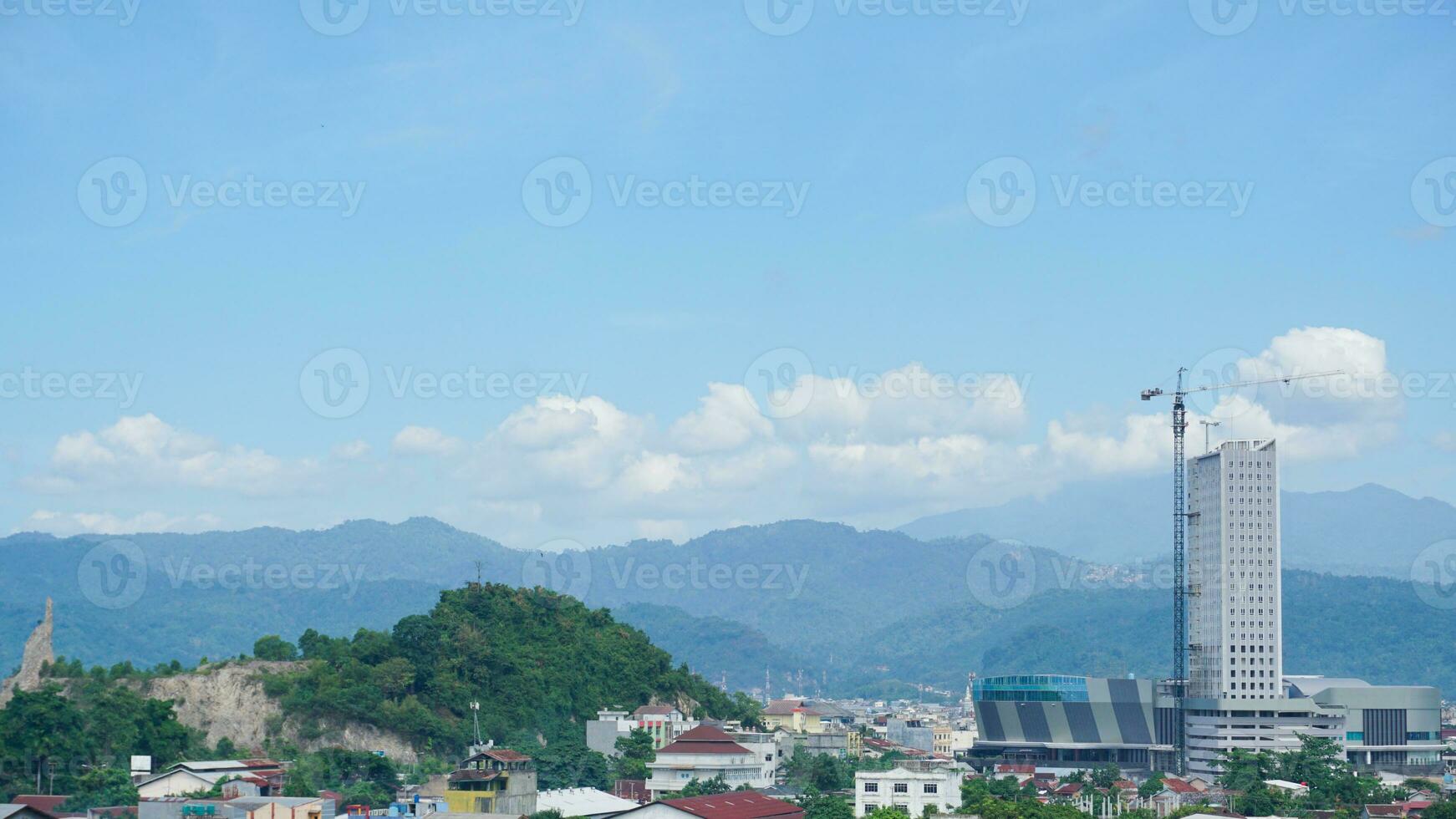Landscape view of a residential building with mountains, blue sky, clouds, sea, and ocean in the background at Lampung. Copy space. Top view of city. Urbanization photo