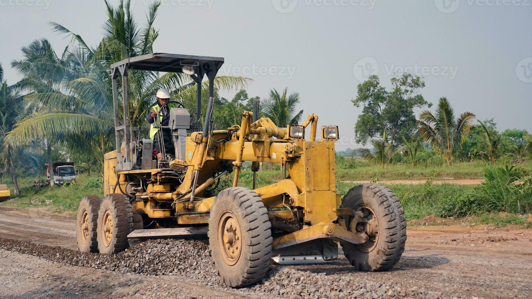 a motor grader leveling stones and gravel for road repairs in Lampung. Front view. photo
