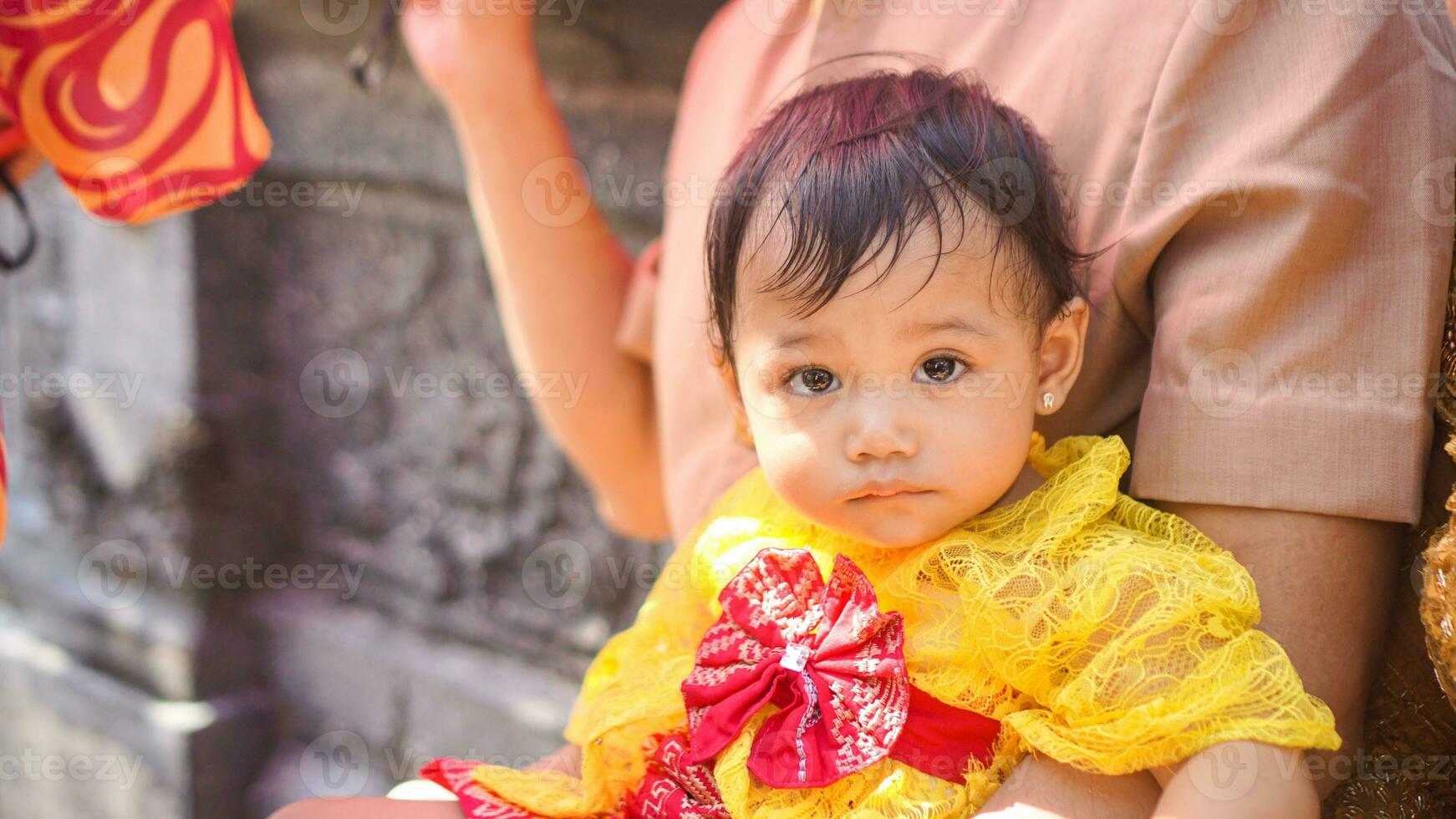 Little cute girl wearing yellow Balinese dress with fanny expression on daddy's lap photo