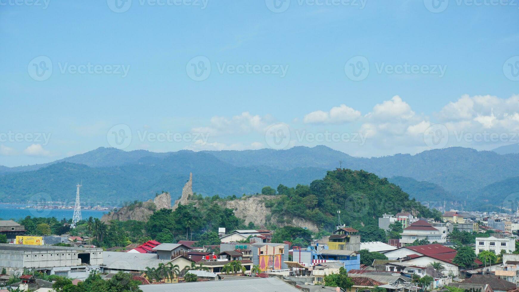 Landscape view of a residential building with mountains, blue sky, clouds, sea, and ocean in the background at Lampung. Copy space. Top view of city. Urbanization photo