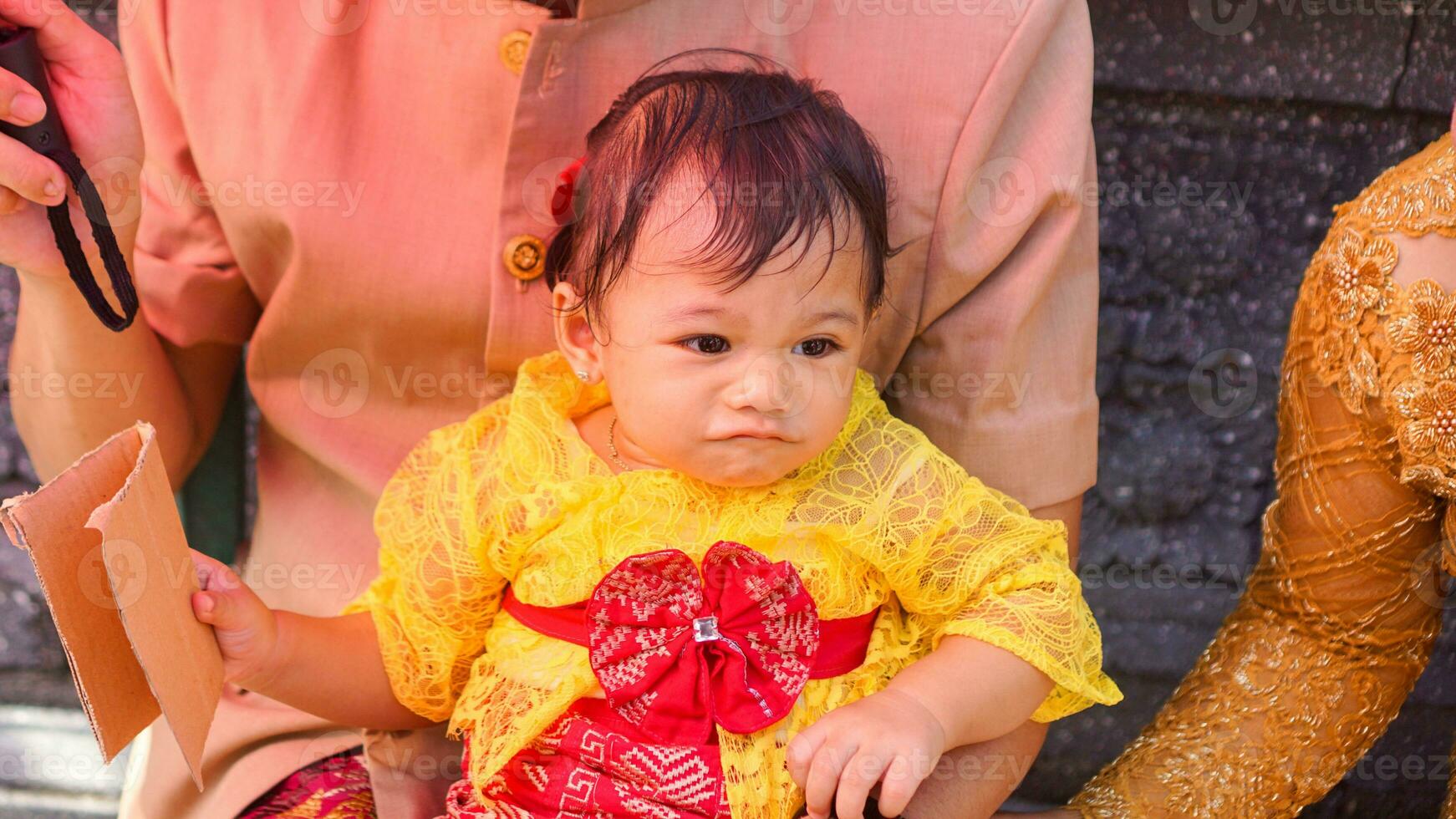 Little cute girl wearing yellow Balinese dress with fanny expression on daddy's lap photo