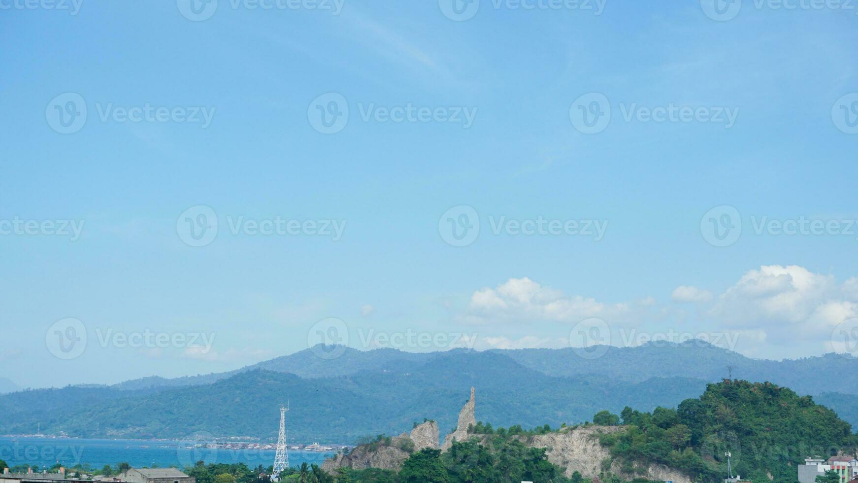 Landscape view of a residential building with mountains, blue sky, clouds, sea, and ocean in the background at Lampung. Copy space. Top view of city. Urbanization photo