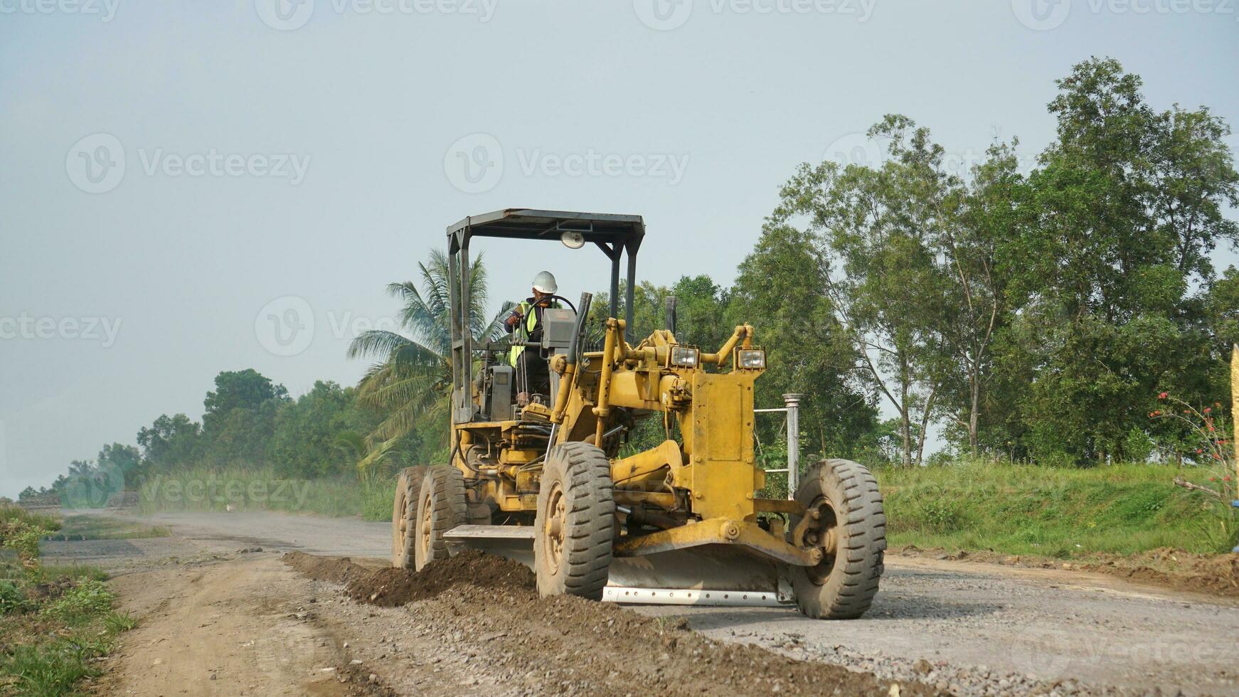 a motor grader leveling stones and gravel for road repairs in Lampung. Front view. photo