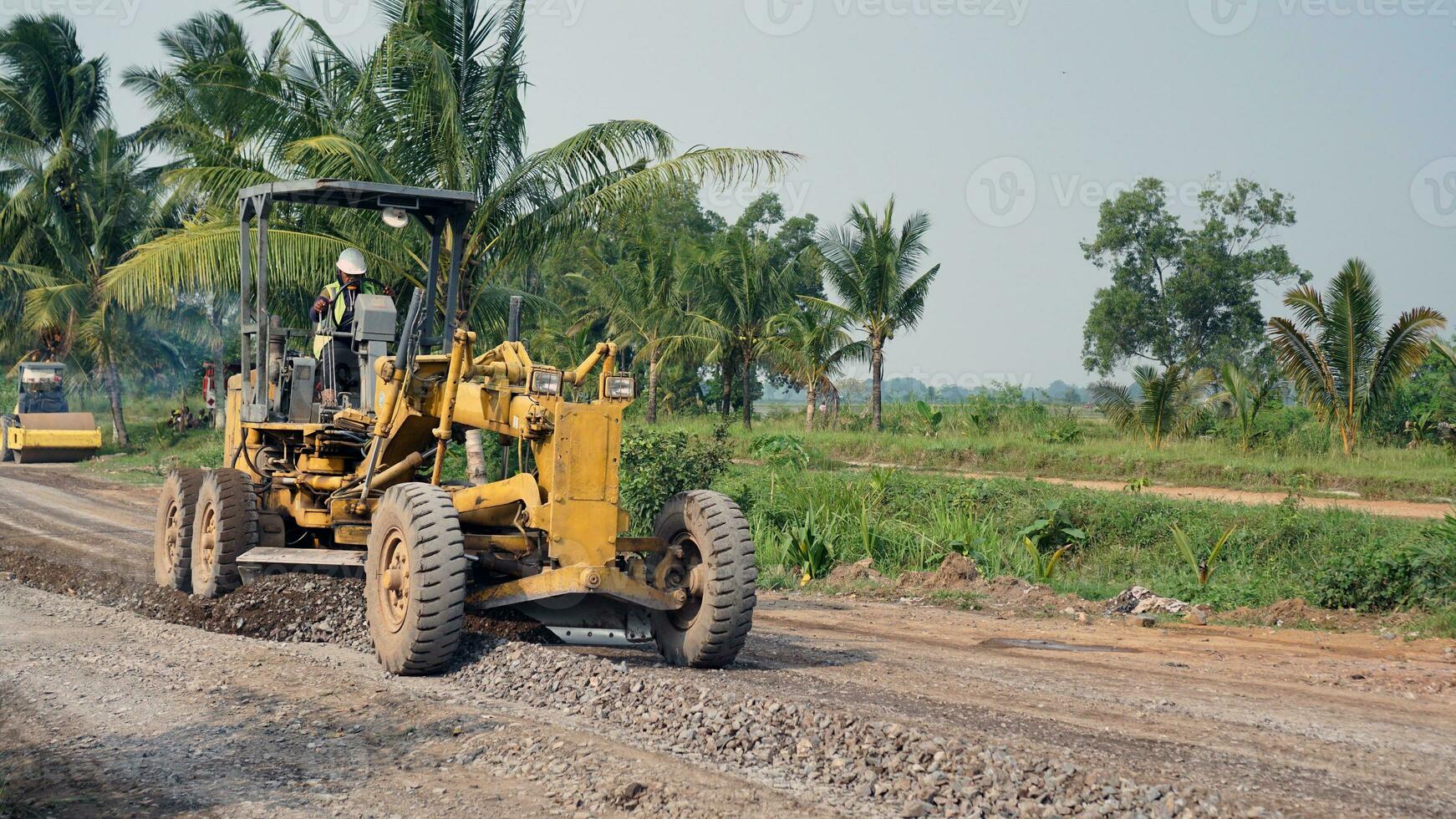 a motor grader leveling stones and gravel for road repairs in Lampung. Front view. photo