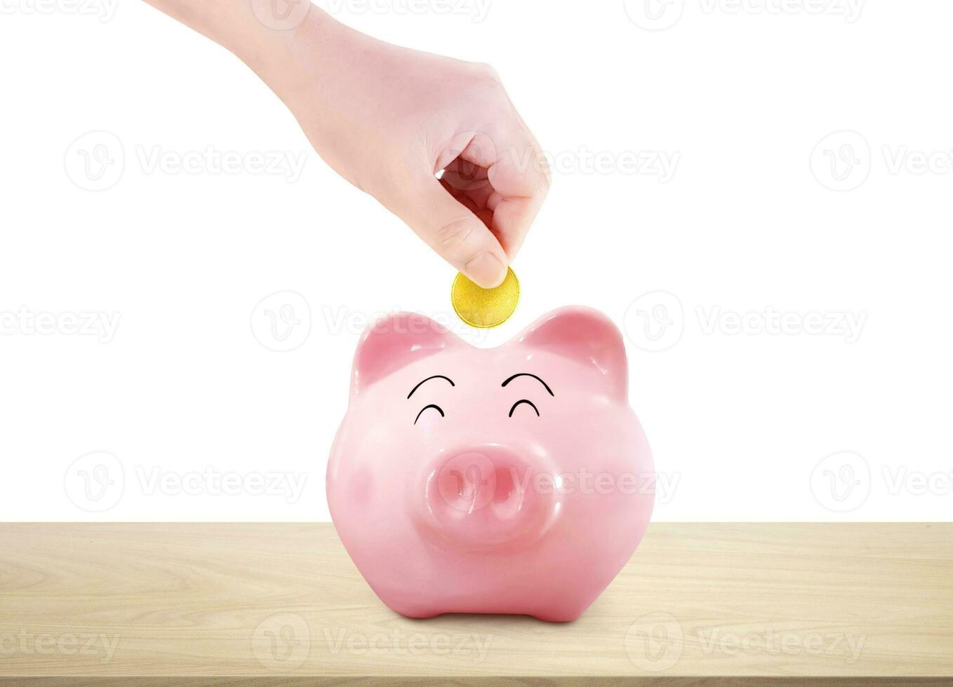 Hand picks up a gold coin and puts it in a piggy bank on a wooden table. white background photo