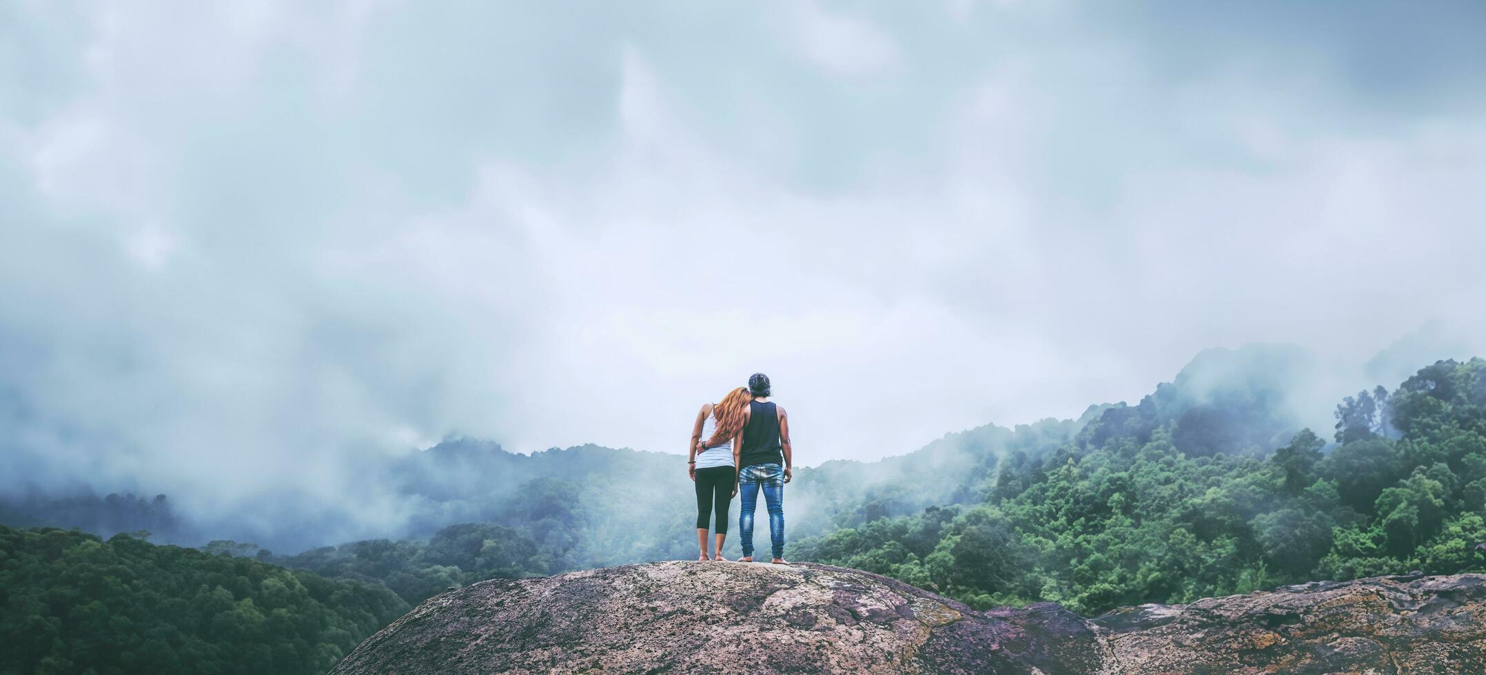 Lover women and men asians travel relax in the holiday. Standing hugged on a rocky cliff. Wild nature wood on the mountain. photo