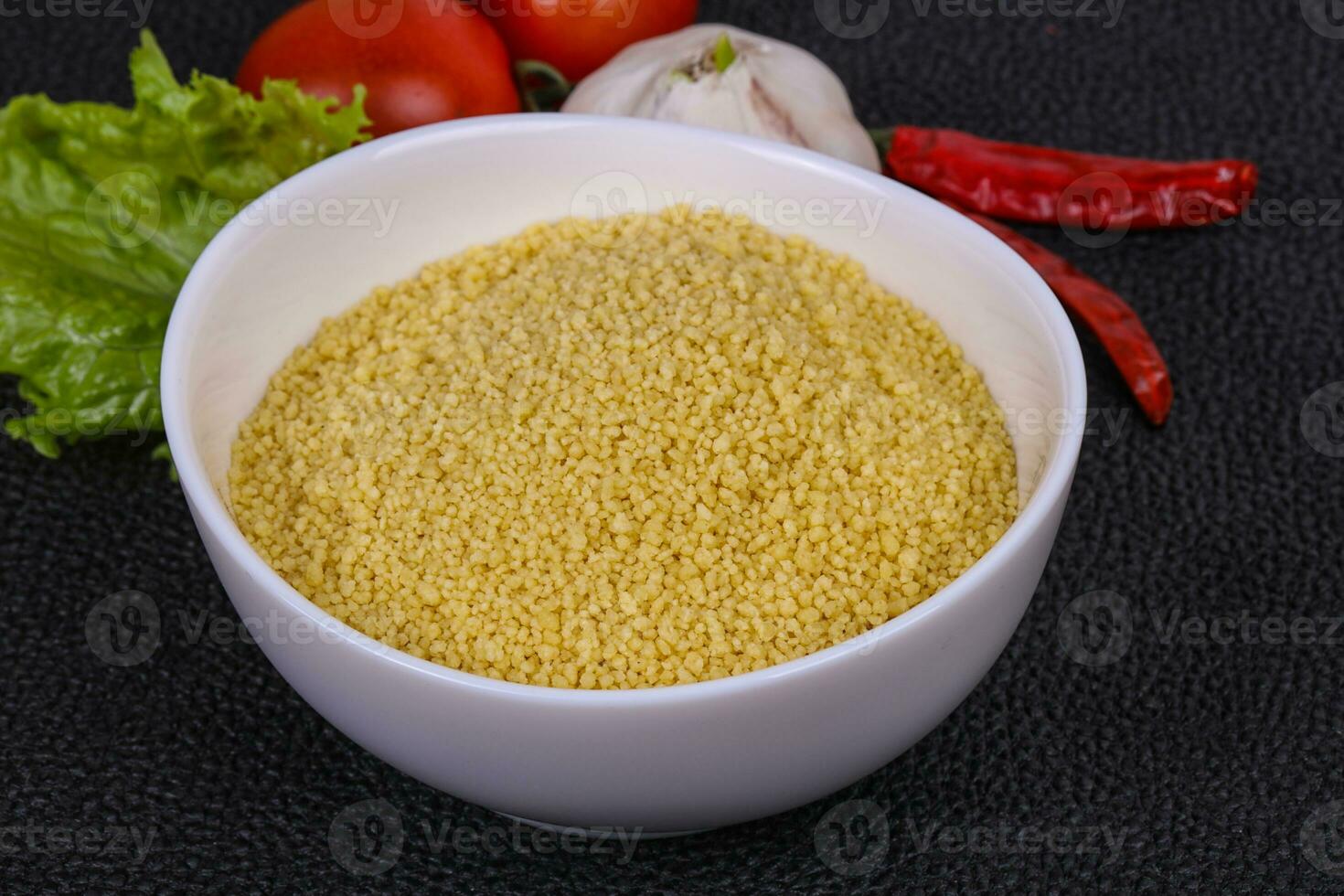 Raw couscous in the bowl served salad leaves, tomato and pepper photo