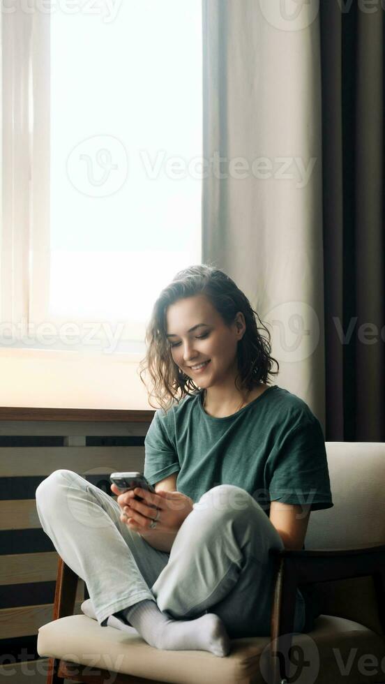 conectado y productivo. joven mujer abraza tecnología, atractivo en comunicación y estudios utilizando teléfono inteligente a hogar. un moderno estilo de vida equilibrio trabajar, estudiar, y conexión mediante móvil aplicaciones foto