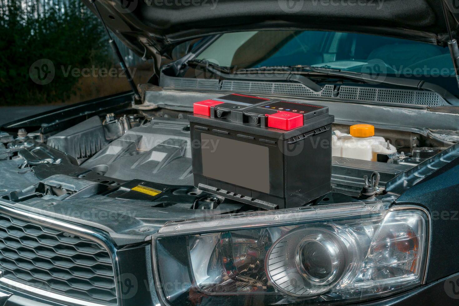 A new battery sits on the engine of a car with the hood open photo