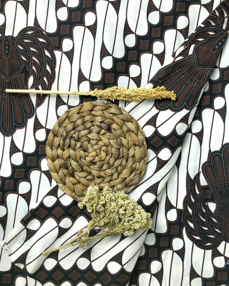 A batik fabric with a rattan mat, a sprig of wheat, and Edelweiss flowers. Nature background. photo