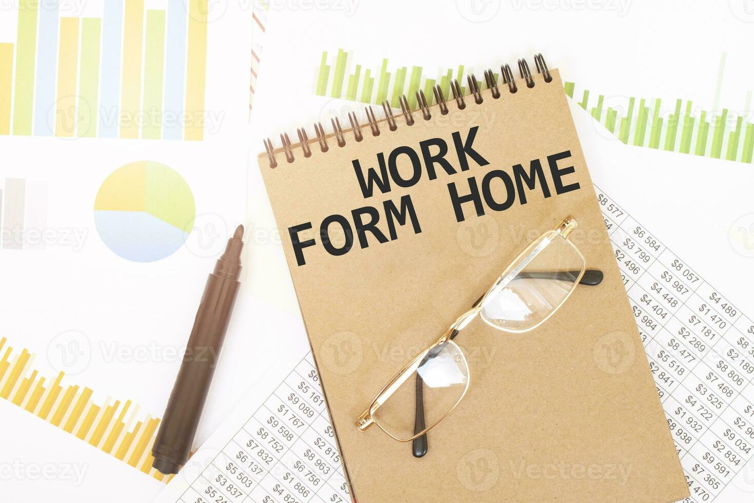 In a craft colour notebook is a WORK FROM HOME inscription, next to pencils, glasses, graphs and diagrams. photo