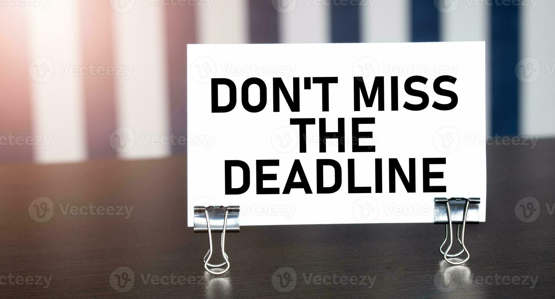 don't miss the deadline sign on paper on dark desk in sunlight. Blue and white background photo