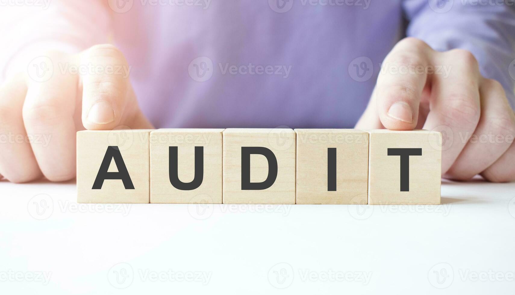 Businessman hand holding wooden cube block with AUDIT business word on table background. photo