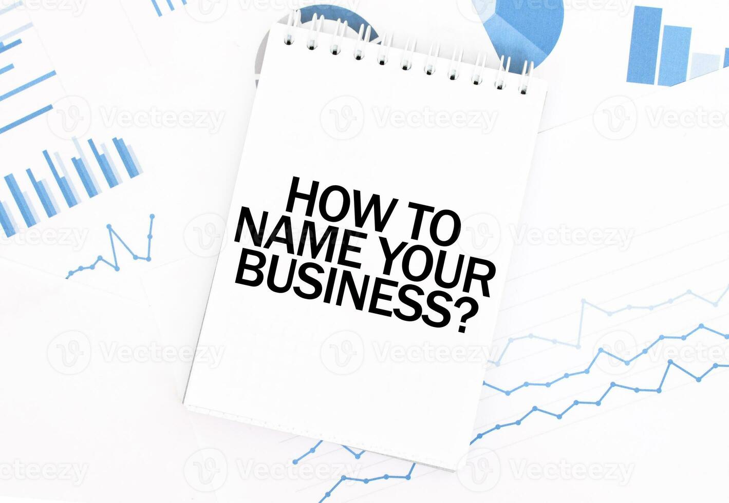 White notepad with text HOW TO NAME YOUR BUISINESS on the financial documentation. Finance and business concept photo