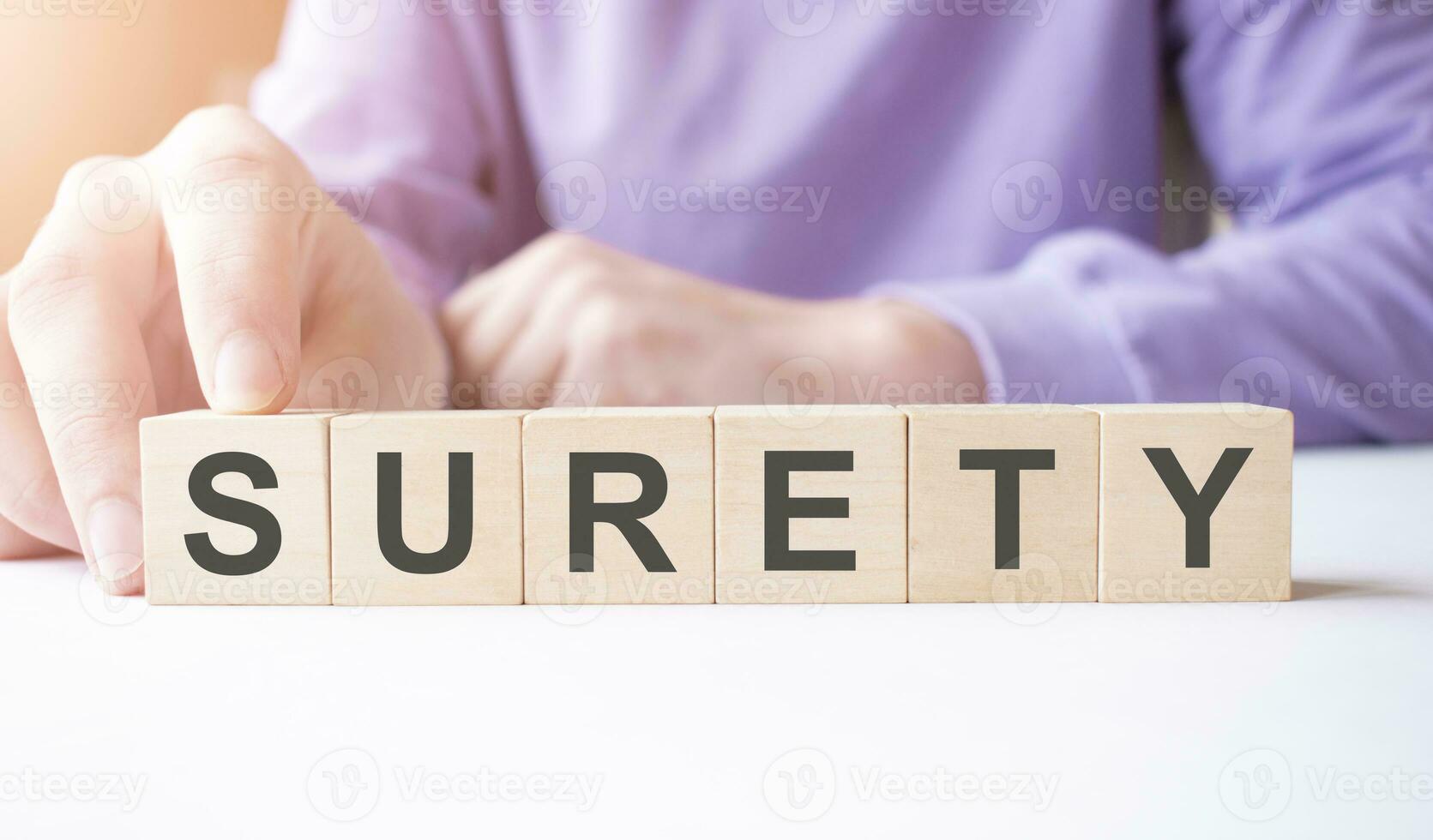 Businessman hand holding wooden cube block with SURETY business word on table background. photo