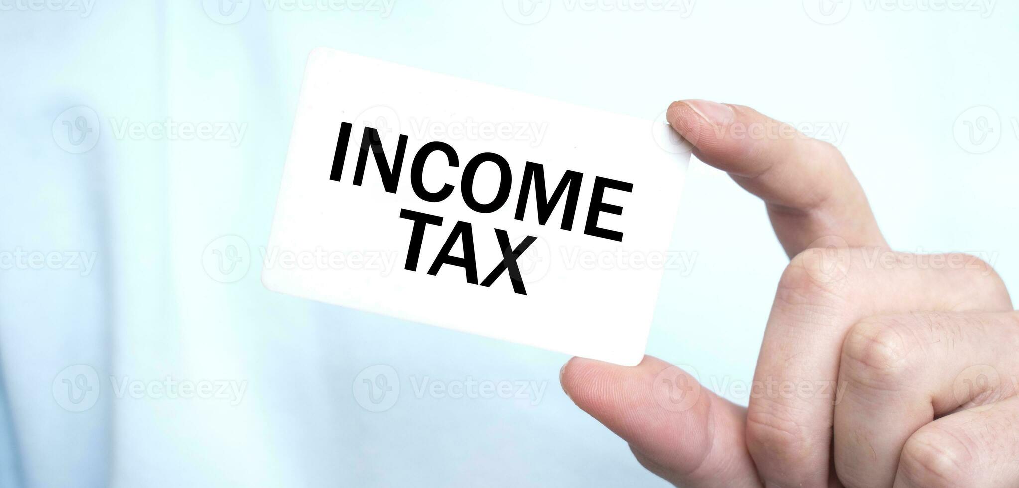 Man in blue sweatshirt holding a card with text INCOME TAX, business concept photo