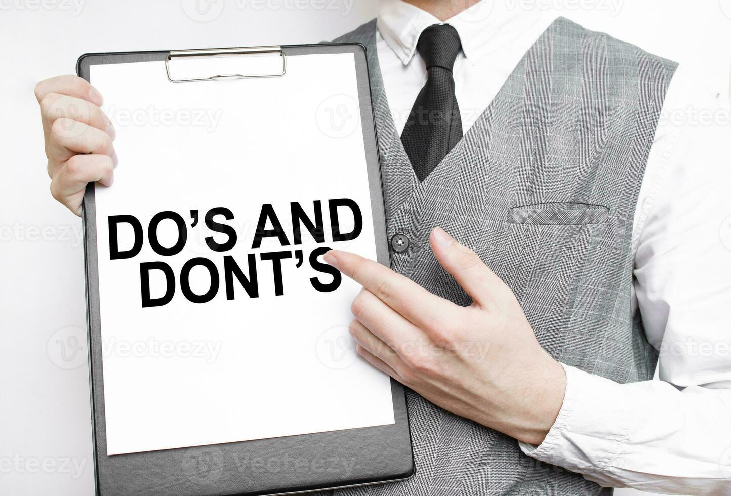 DO's and DONT's inscription on a notebook in the hands of a businessman on a gray background, a man points with a finger to the text photo