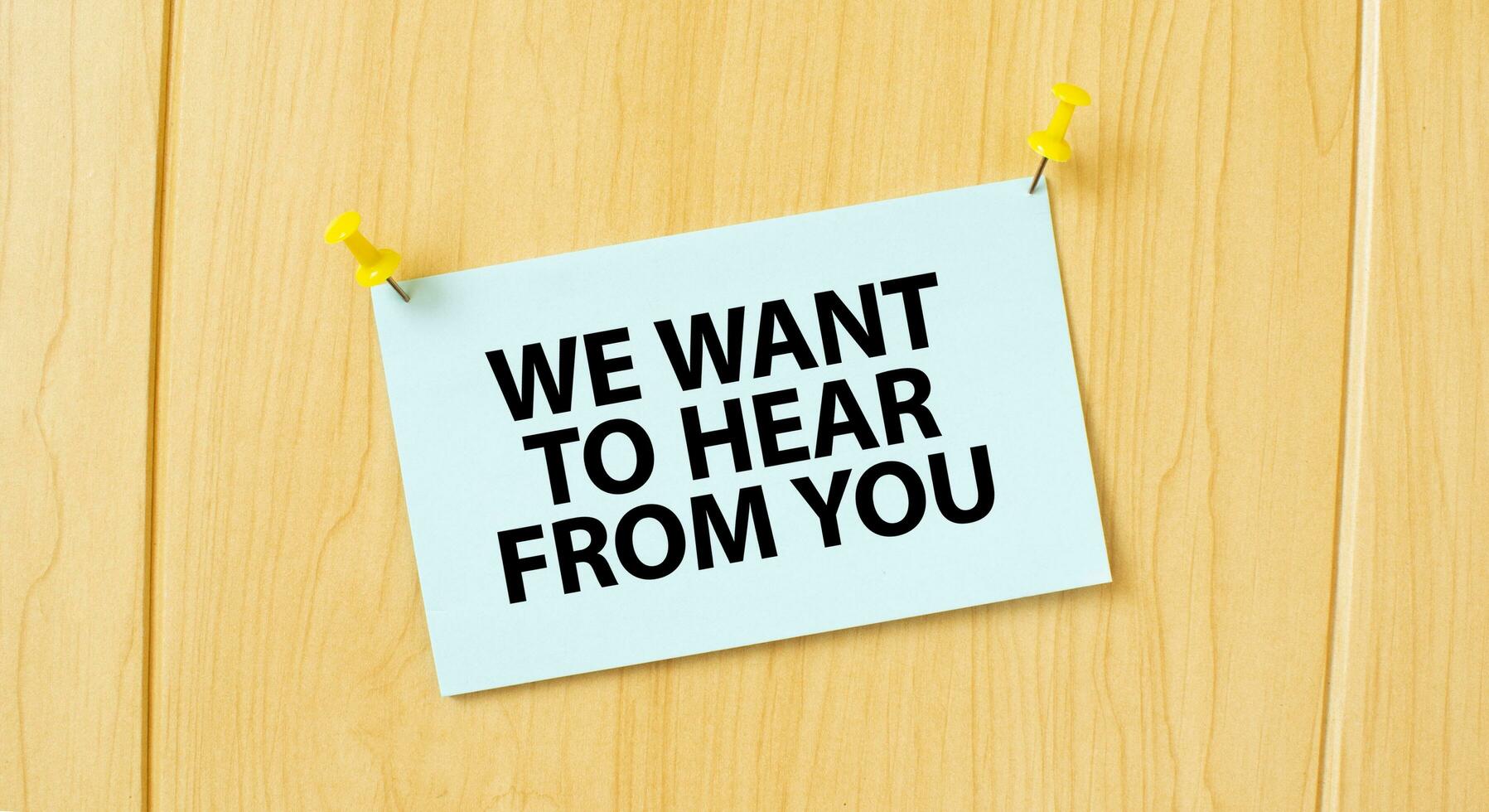 WE WANT TO HEAR FROM YOU sign written on sticky note pinned on wooden wall photo