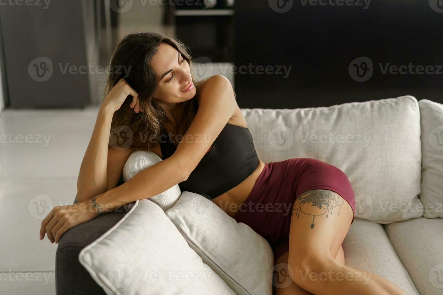 Pretty  brunetre woman sitting on cozy sofa  in stylish modern interior.  Wearing stylish sport clothes. photo