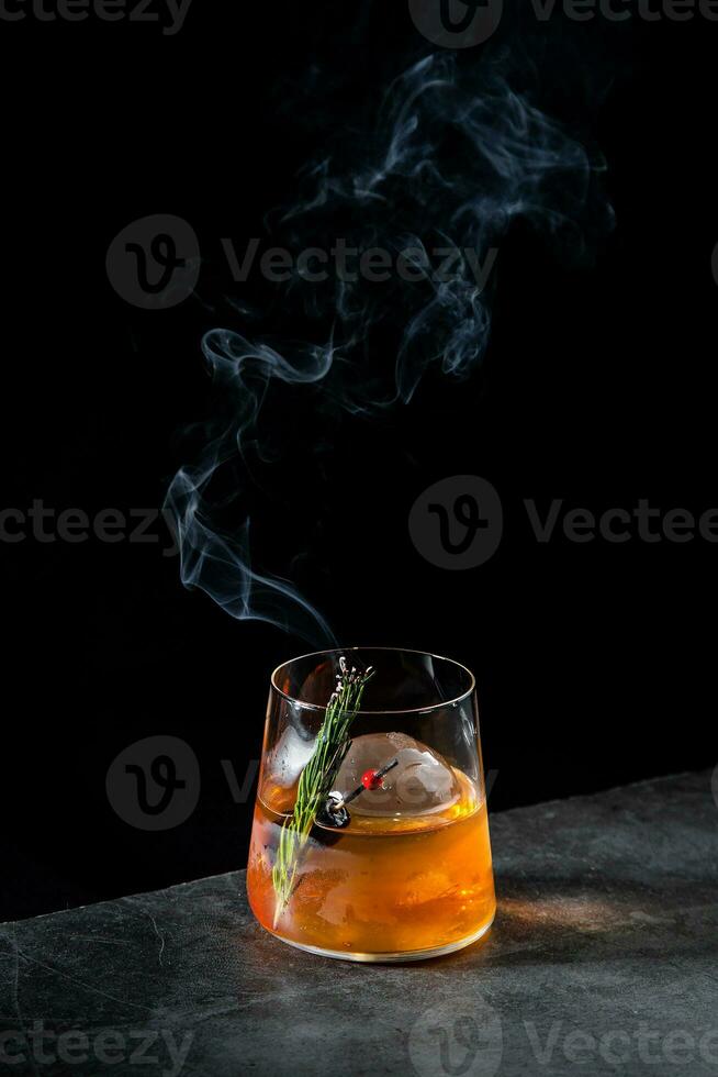 aromatic cocktail with a sprig of pine needles and round ice on a dark background, side view photo