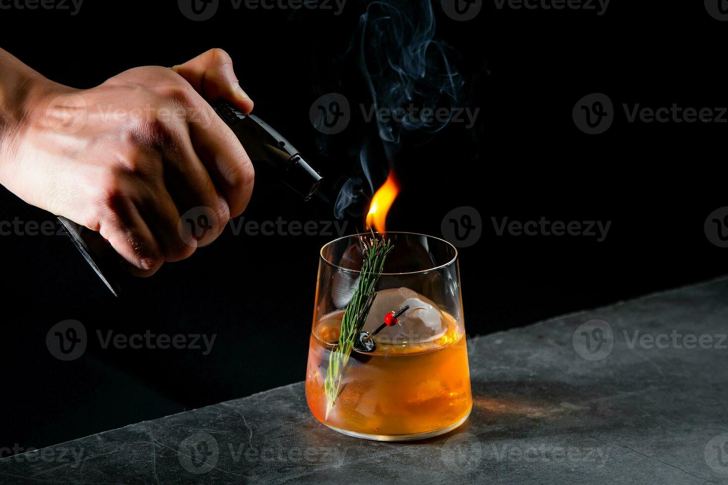 aromatic cocktail with a sprig of pine needles and round ice on a dark background, side view photo