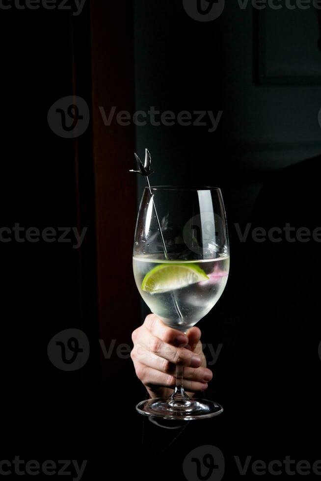 transparent cocktail with lime in a wine glass on a dark background side view photo