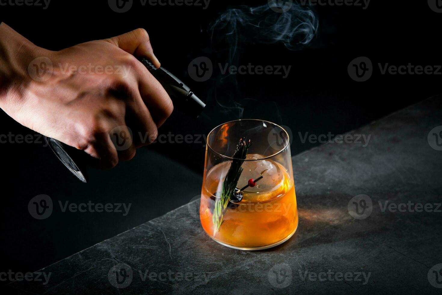 aromatic cocktail with a sprig of pine needles and round ice on a dark background, side view photo