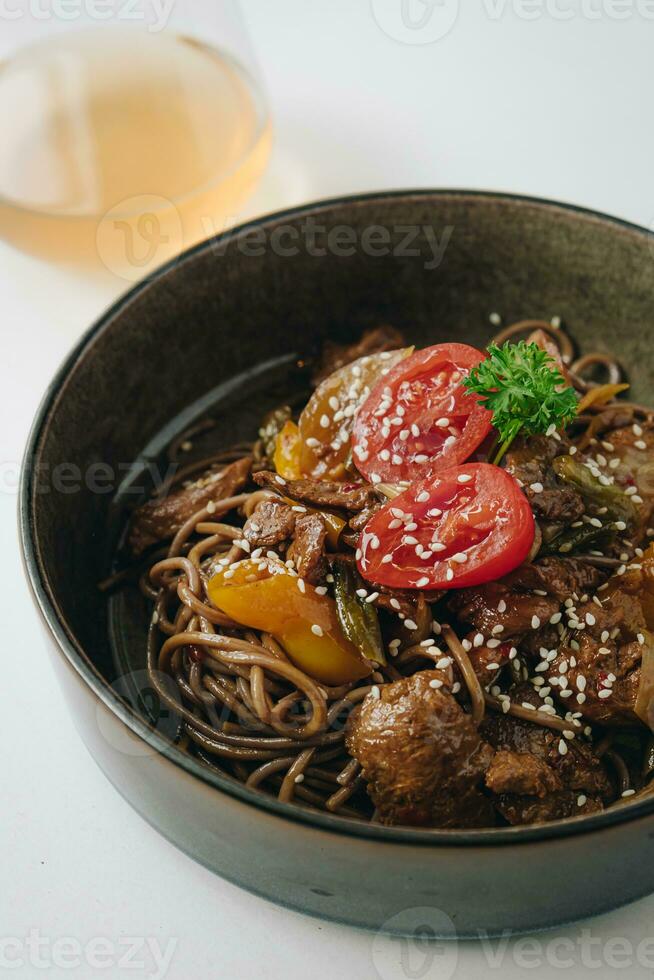 noodles with beef, vegetables, cherry tomatoes and sesame sauce in a deep plate side view photo