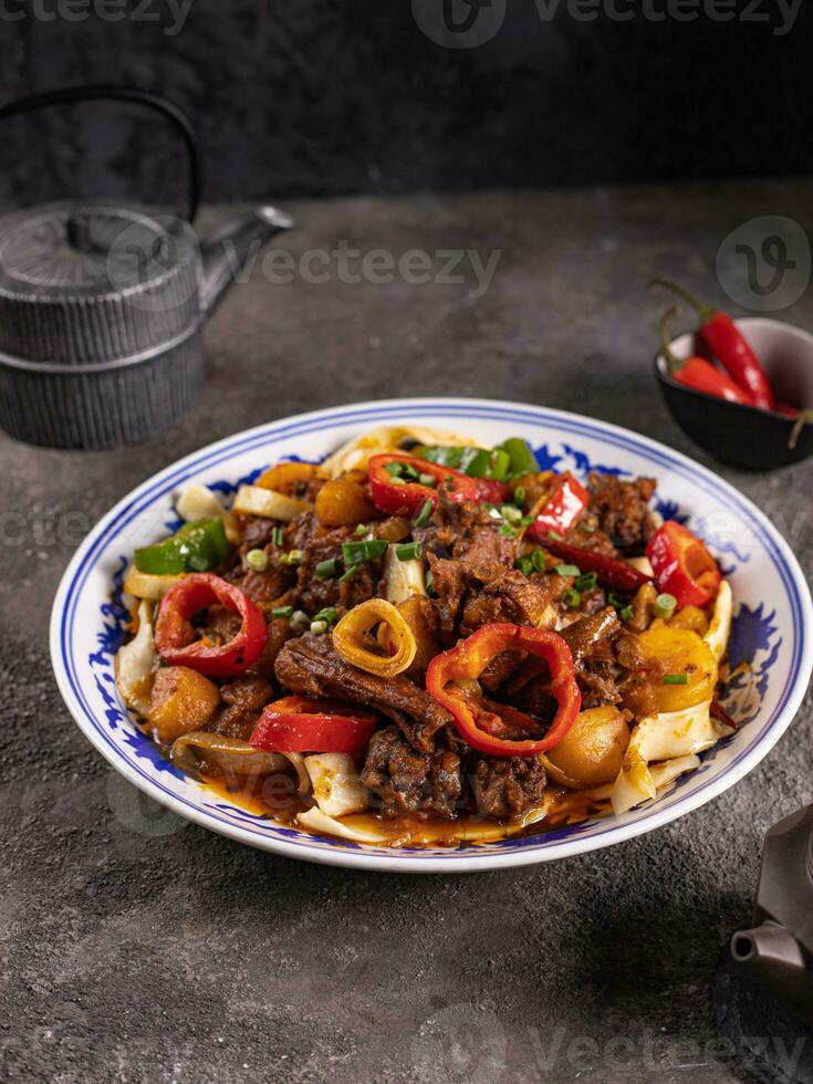 noodles with bell pepper, potatoes, meat and herbs in a plate with a pattern side view photo