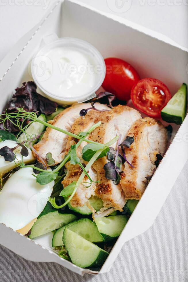 piezas de pollo con verduras, hierbas y salsa en un caja de almuerzo foto