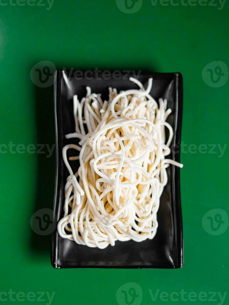 dry and raw flour noodles on a black plate and a green background. View from above. ingredient for hotpot photo