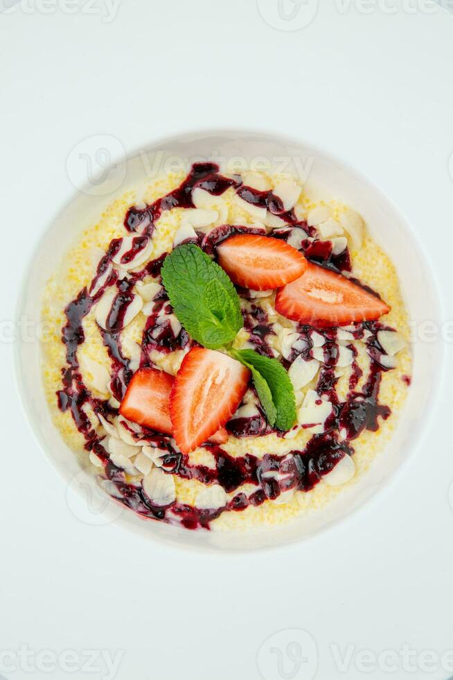 porridge with strawberries, mint and berry jam in a white plate, top view photo