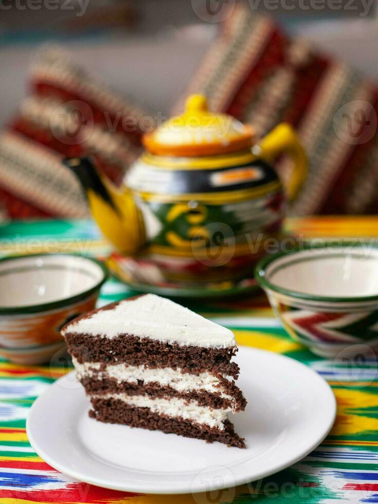 postre chocolate pastel con blanco mantequilla crema en oriental estilo en un techo con un tetera y un taza para té. foto