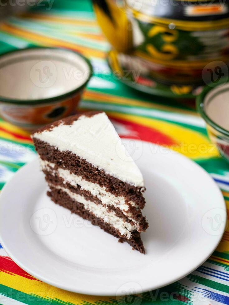 postre chocolate pastel con blanco mantequilla crema en oriental estilo en un techo con un tetera y un taza para té. foto