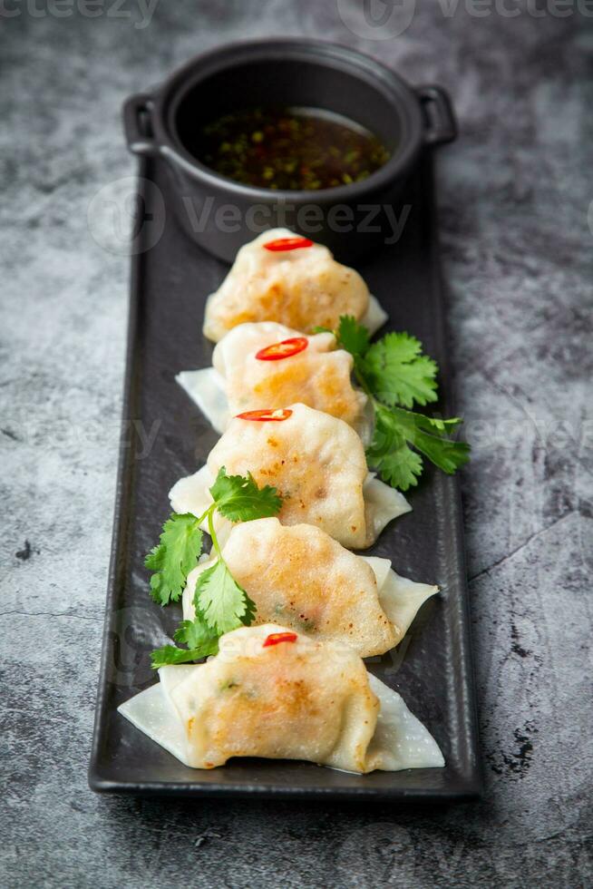 Asian dumplings with soy sauce, chili peppers and herbs on a dark background side view photo