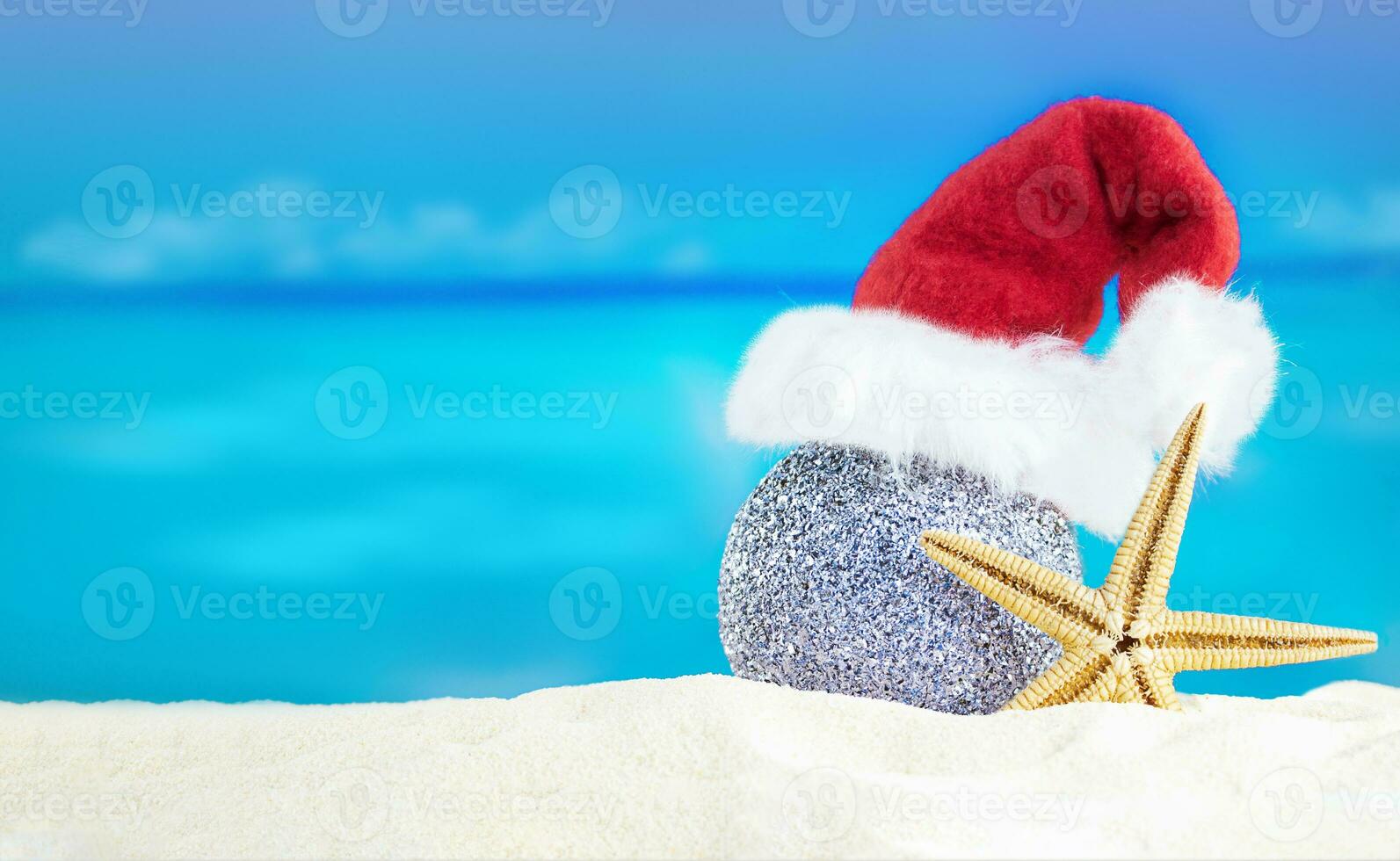 Shiny silver ball in Santa's hat with starfish on sand of beach. Christmas, New Year. Copy space photo