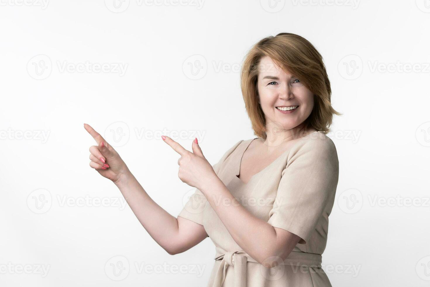 European blonde woman adult in beige dress looking at camera on white background with fingers raised photo