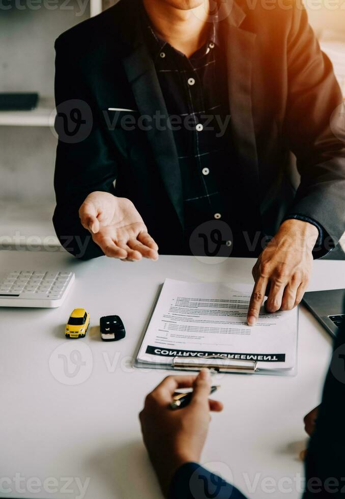 A car rental company employee is handing out the car keys to the renter after discussing the rental details and conditions together with the renter signing a car rental agreement. Concept car rental. photo