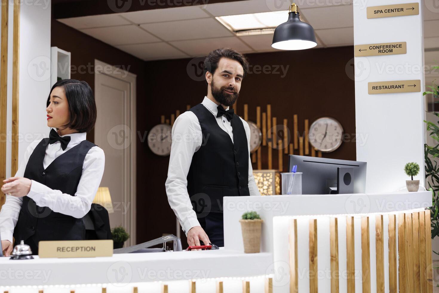 Elegant hotel employee at front desk working on booking enquiries and room reservations with records and computer. Reception staff preparing to welcome guests at luxury resort. photo