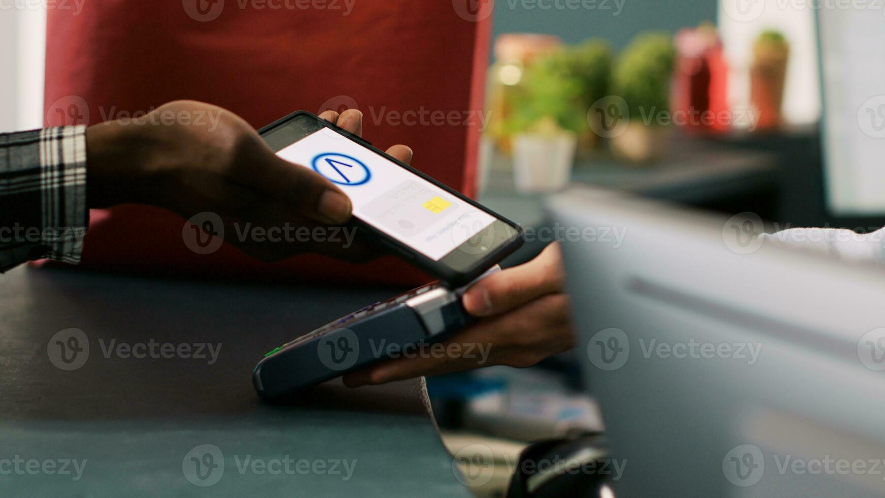 Customer paying with mobile phone at pos terminal at fashion store counter desk, buying fashionable clothes. African american man shopping for casual wear in modern boutique. Fashion concept photo