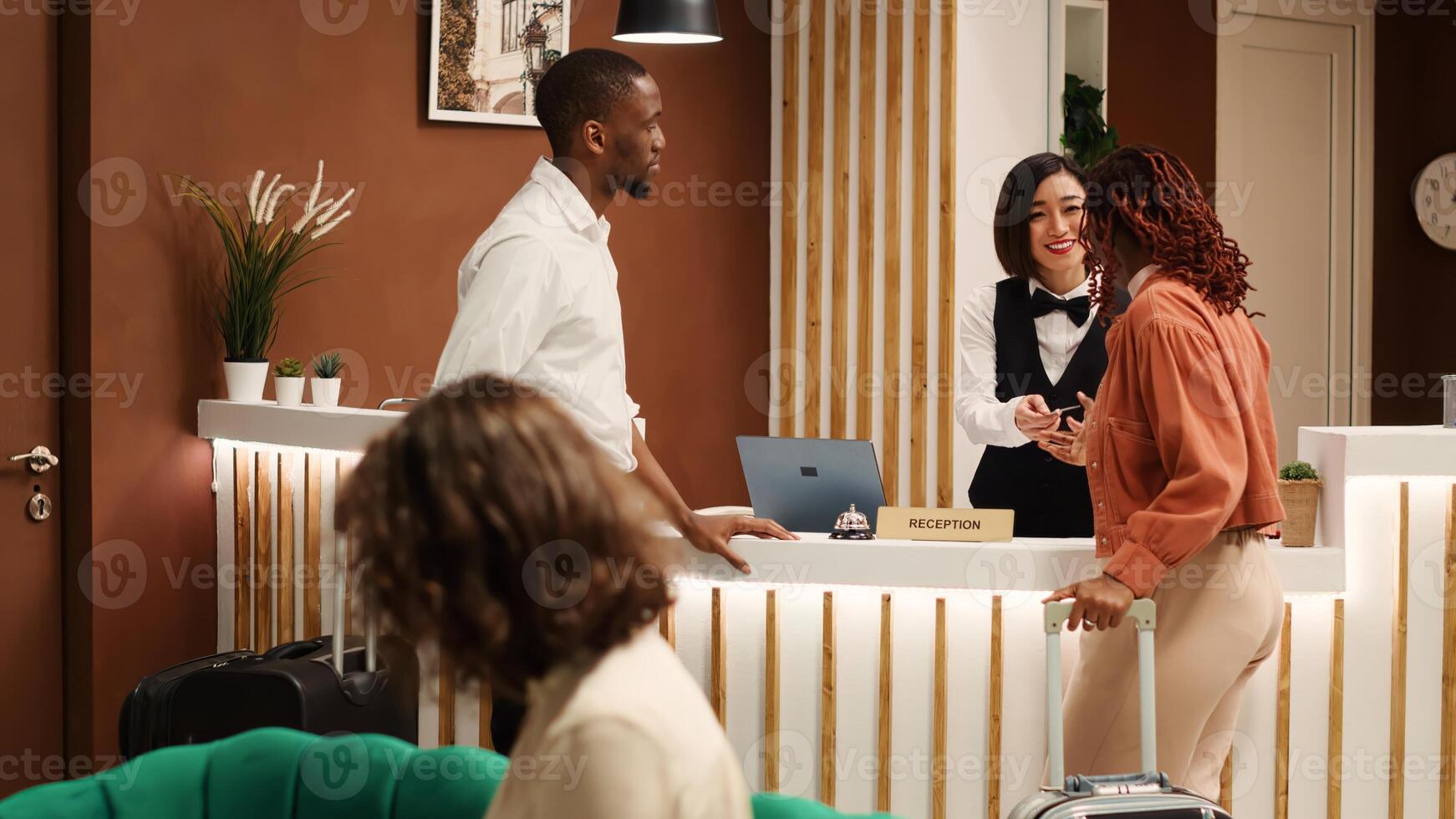 Happy receptionist handing company executives room access key card during check in process. Cheerful guests on business trip and professional hotel employee chatting in elegant resort lounge photo