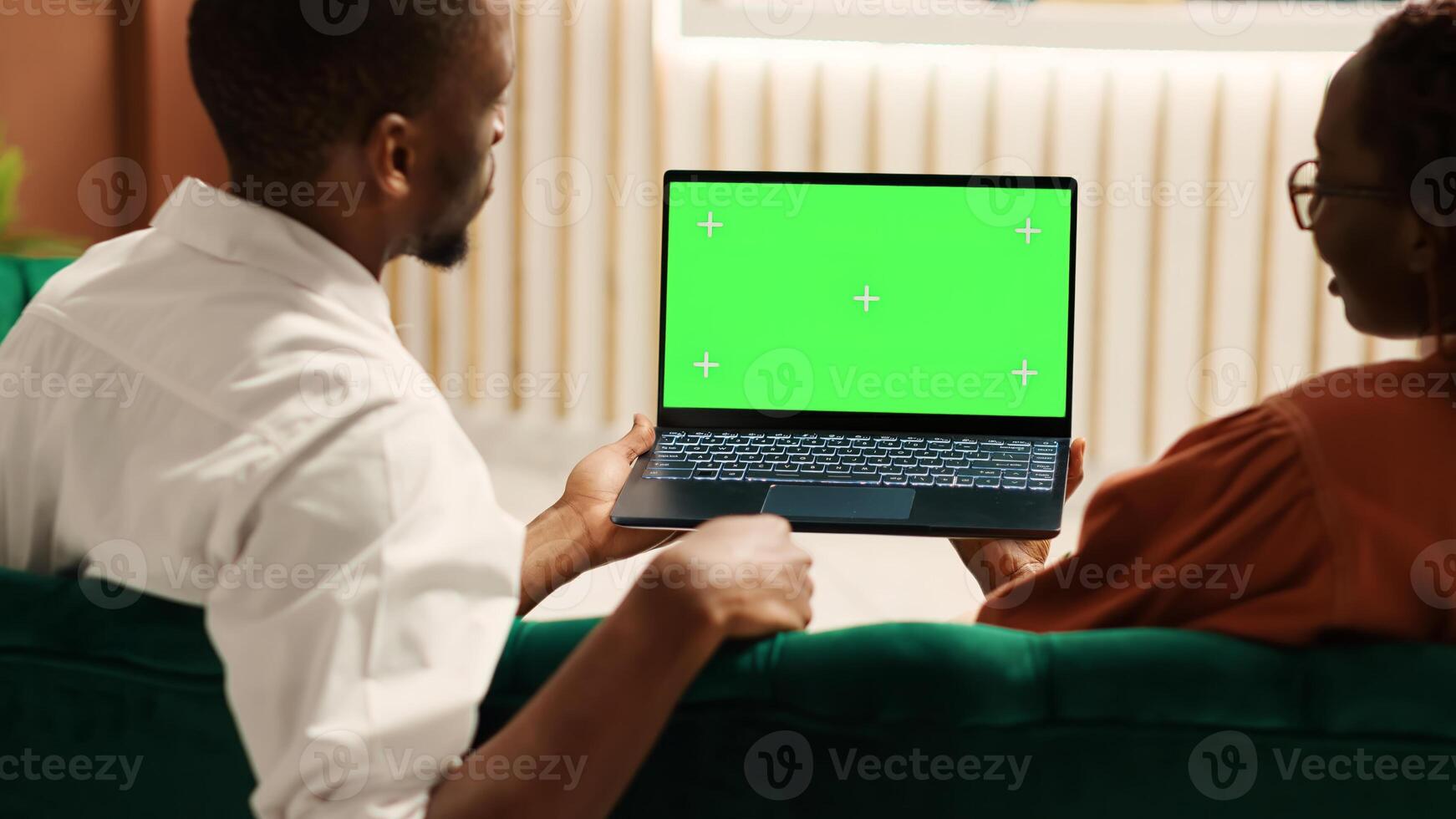 Bored tourists watching video on laptop chroma key green screen mock up waiting for check in process to be over. Guests sitting in hotel foyer while porter employee carries luggage to their room photo