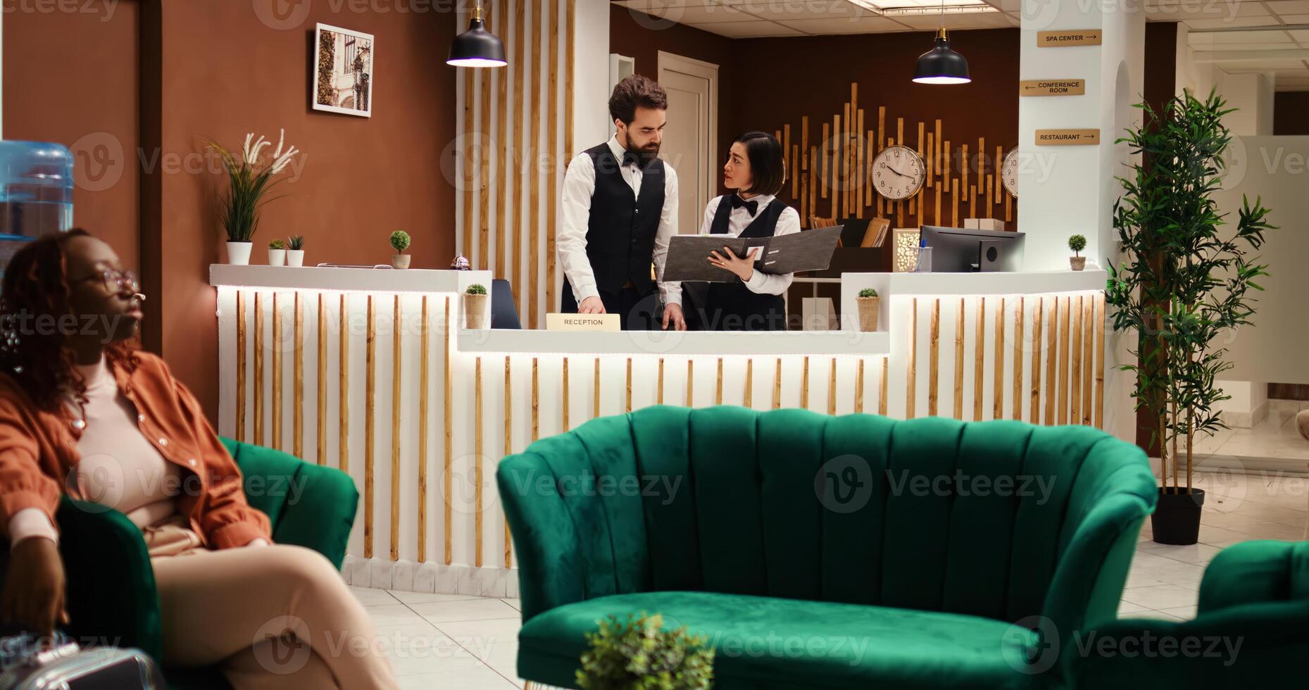 Hotel manager ready to discuss holiday package options and amenities upgrade with tired tourist after long flight. Resort staff employees preparing guest room, working in stylish reception lobby photo