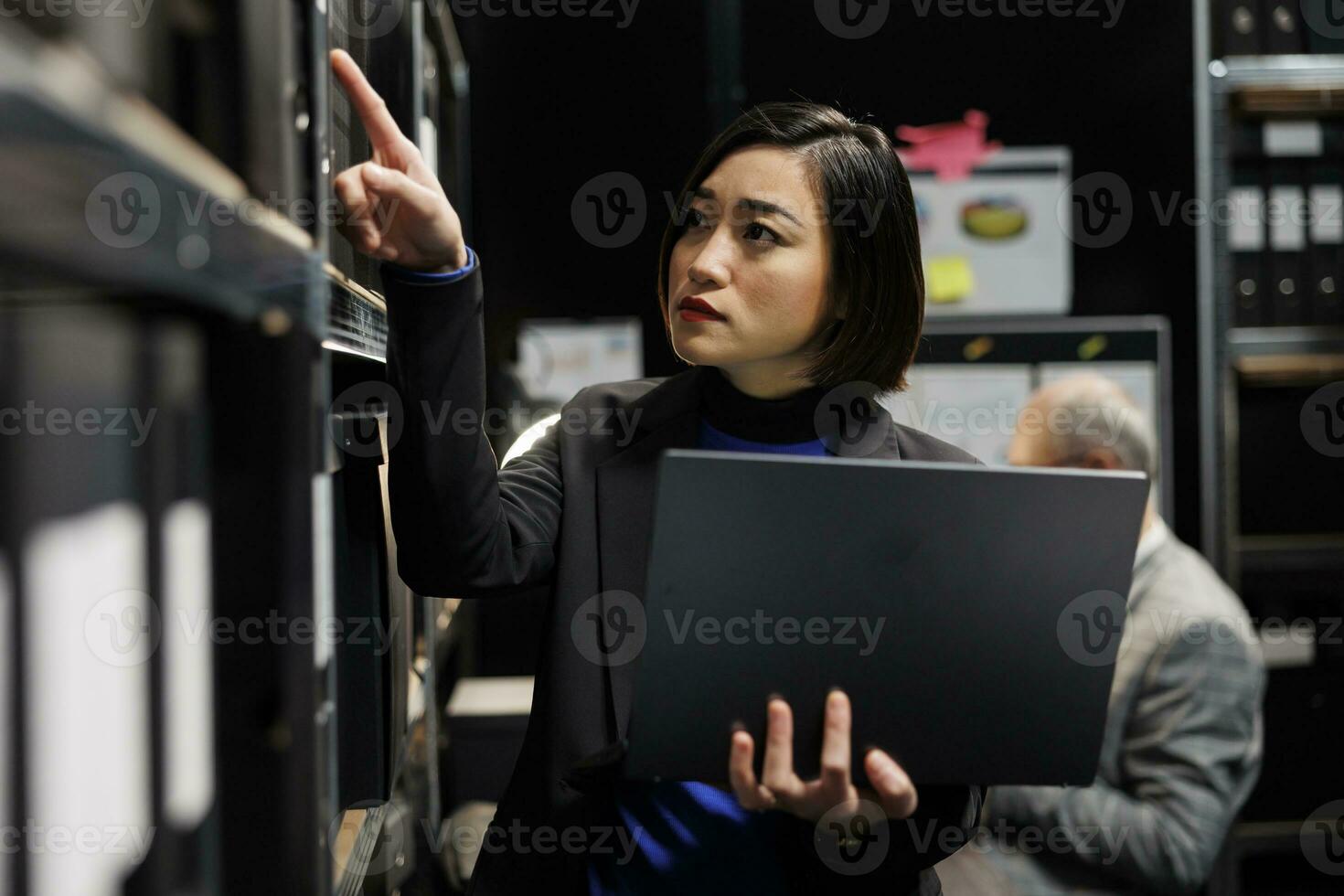 Asian private investigator in criminal cases archival depository office looking for criminal case paperwork on cabinet shelves. Detective surrounded by criminology file folders in agency cabinet room photo