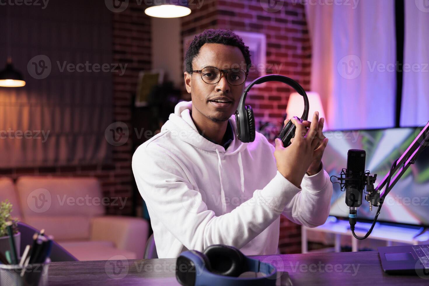 Portrait of african american tech vlogger reviewing headphones in living room studio. Entertaining content creator filming technology channel vlog for audiophiles, presenting info photo