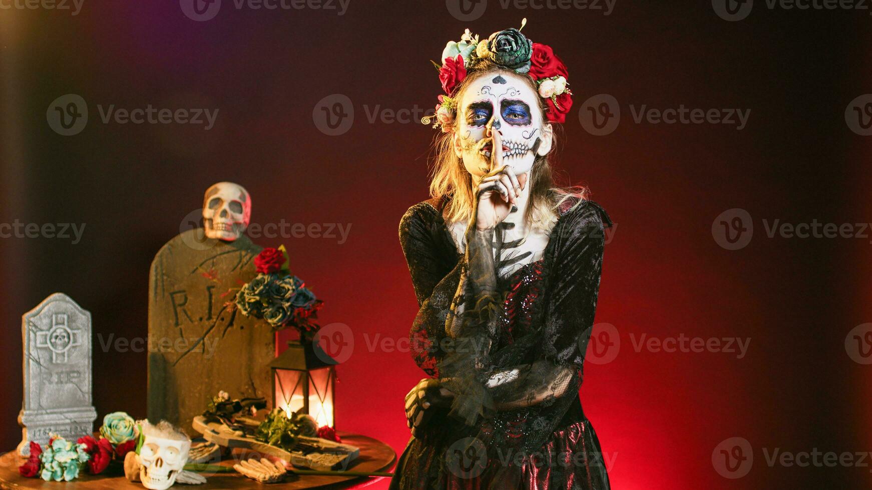 Young scary woman doing hush gesture to keep secret, wearing santa muerte costume and showing slience mute and secrecy sign with finger over lips. Holy dios de los muertos holiday. photo