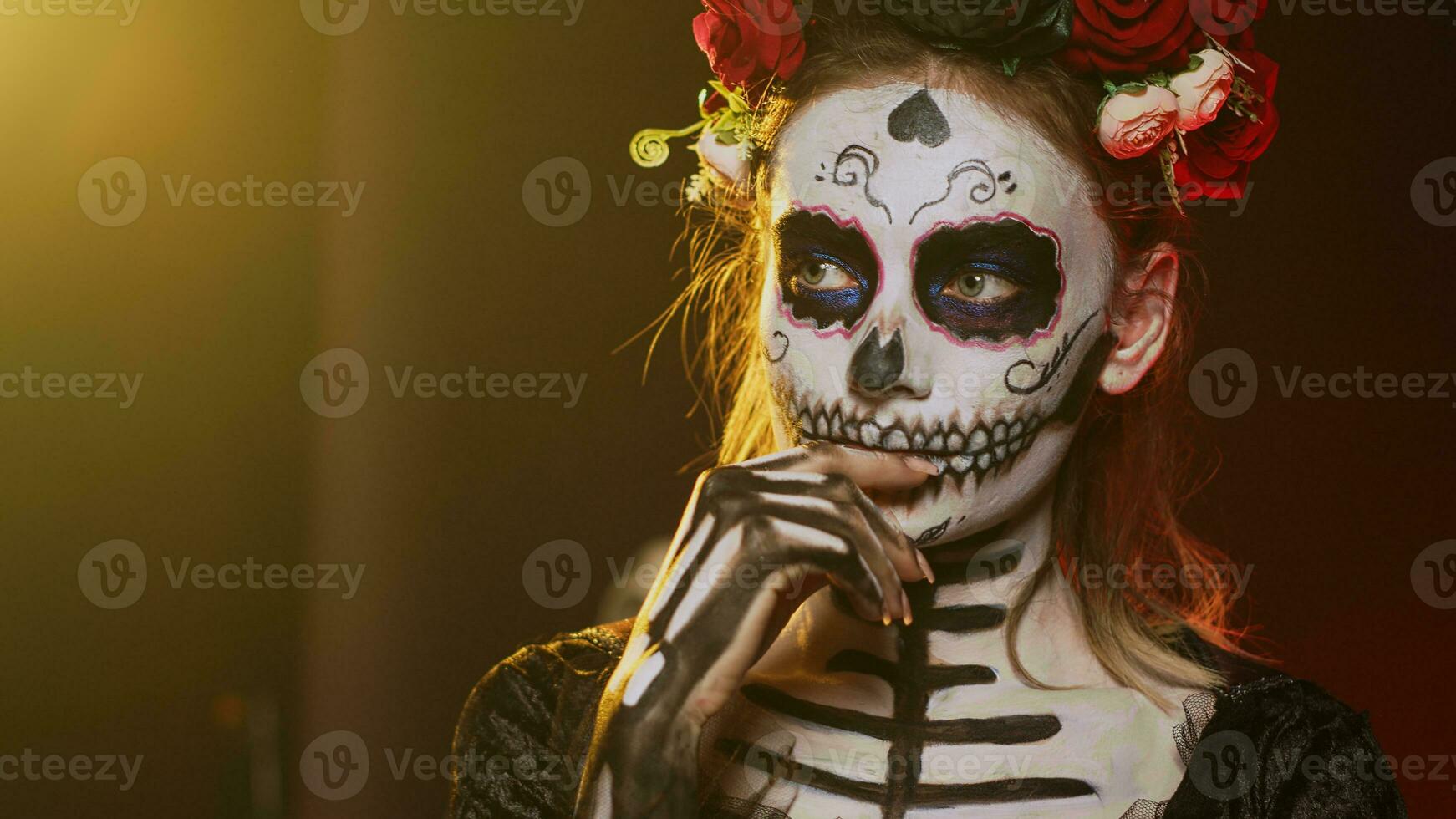 Scary young adult thinking about santa muerte in studio, acting thoughtful and pensive on day of the dead mexican holiday. Woman portraying holy cavalera catrina halloween goddess. Handheld shot. photo